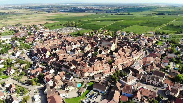 View of Eguisheim commune from air, green wine fields on background. Scenic aerial panorama of small historical village at Alsace, part of famous Alsatian Vineyard Route
