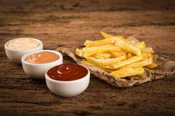 French fries with sauces on rustic wooden background