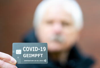 Älterer Herr zeigt Impfnachweis auf einer Chipkarte, die eine COVID-19 Impfung nachweist.