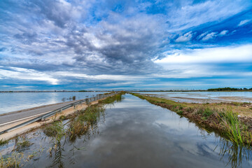 Flooded road and canal under stormy and cloudy sky