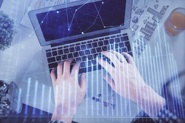 Double exposure of man's hands typing over laptop keyboard and forex chart hologram drawing. Top view. Financial markets concept.