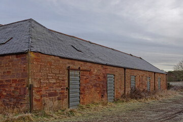 Fototapeta na wymiar Part of an old Agricultural Farm Store Complex with metal shutter doors built into the red Stone Building on an abandoned Golf Course near Arbroath.
