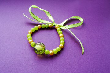 women's bracelet from green beads of different sizes tied with satin ribbon lies on a lilac background side view