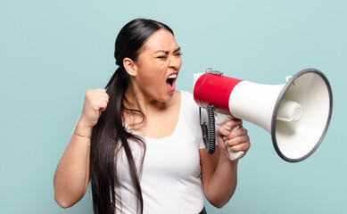 hispanic woman shouting aggressively with an angry expression or with fists clenched celebrating...