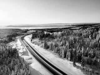 Highway with cars driving through a mountain pass with snow covered trees.