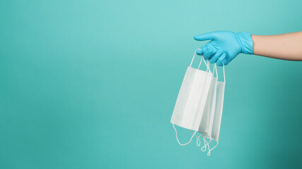 Hand holding white mask or face masks wear medical gloves or latex gloves on green and blue or Tiffany Blue background.