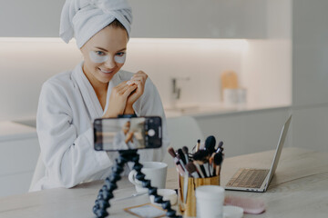 Pleased beauty blogger sits in front of cellphone camera shares experience about skin care wears...