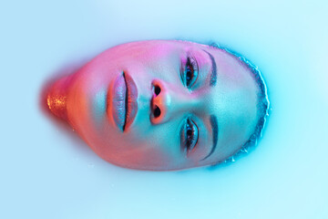 Make up. Beautiful female face in the milk bath with soft glowing in blue-pink neon light. Copyspace for advertising. Modern neoned colors, foam. Beauty, fashion, style, skincare concept. Attractive.