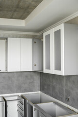Custom kitchen cabinets installation with a white furniture facades mdf. Gray modular kitchen from chipboard material on a various stages of installation. A frame furniture fronts mdf profile.