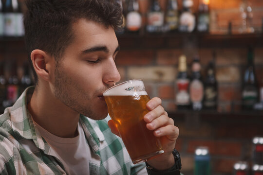 Close up of a handsome young man sipping beer from his glass at beer pub - Powered by Adobe