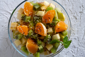 Bowl of healthy salad from fruit with green mint on a white table. Mixed fresh banana, orange, kiwi, fruit. copy space. Healthy vegan lunch. top view