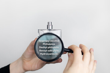 A woman examines the harmful ingredients of the perfume through a magnifying glass. Means with isopropyl alcohol, phthalates, diethyl phthalate, benzyl salicylate, hydroxyanisole.