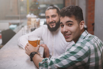 Young handsome man smiling to the camera, enjoying drinks with his friend at beer pub