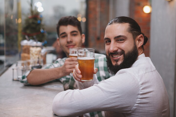 Happy bearded man smiling to the camera, holding up his beer glass at the pub
