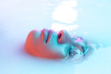 Surface. Beautiful female face in the milk bath with soft glowing in blue-pink neon light....
