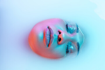 Delighted. Beautiful female face in the milk bath with soft glowing in blue-pink neon light. Copyspace for advertising. Modern neoned colors, foam. Beauty, fashion, style, skincare concept. Attractive