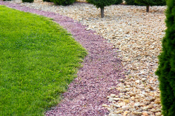 Landscaping of a backyard garden with yellow and red stone mulching way on a day summer park...