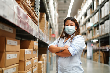 Fototapeta na wymiar Fat woman worker inspecting stock of products while working in large warehouse. face mask during coronavirus and flu outbreak. Virus and illness protection
