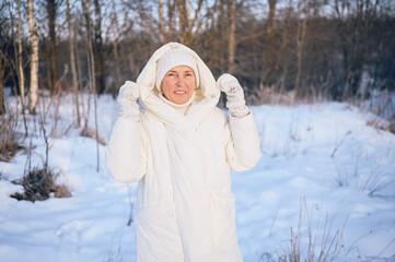 Happy elderly senior mature woman in white warm outwear playing with snow in sunny winter outdoors. Retired healthy people holiday vacation winter activities, active lifestyle concept.