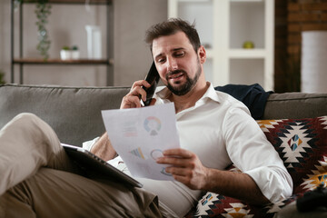 Young man working from home. Businessman at home on sofa with laptop and phone