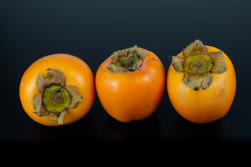 Tropisches Obst: Drei exotische Kaki Früchte auf einem schwarzen Hintergrund