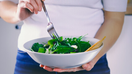 Eating salad, woman standing eats a meal of salad. Fresh and light lunch. Organic vegetable, natural ingredients for healthy nutrition. Eating green food. Cooking vegetable