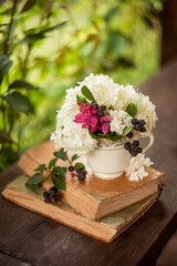 white hydrangea with berries and books in a tea mug. flowers in a tea mug. garden aesthetics. summer holidays and gardening.