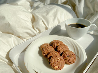 black coffee in the hot white cup in tray and blanket on the bed as a breakfast in bed in winter. Concept lazy weekend morning of a lover with light from sunrise with warm drink and beverage.