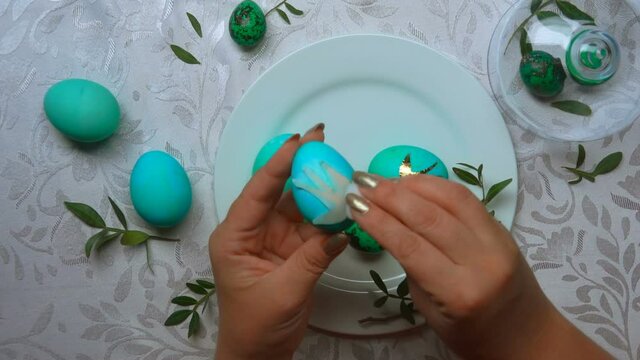 Easter preparations: female hands are decorating green-colored easter eggs with a foil bird image