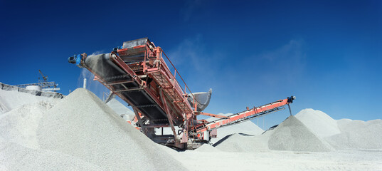 Working mobile crusher machine on the background of crushed stone hills and blue sky, close-up panorama.