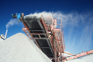 Conveyor belt of a working mobile crusher, close-up, with blown away by the wind white stone dust...