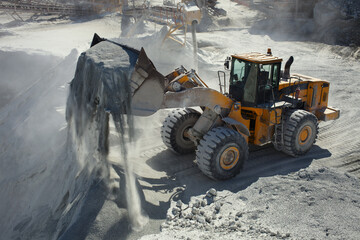 Front end loader pours out a small stone fraction from the bucket against the background of the equipment of the ore-dressing plant, close-up.