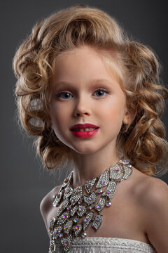 portrait of a beautiful little blonde with jewelry and stylish hairstyle, wearing a white dress