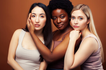 young pretty asian, caucasian, afro woman posing cheerful together on brown background, lifestyle diverse nationality people concept