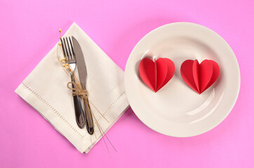 plate with two paper hearts on pink background with cutlery