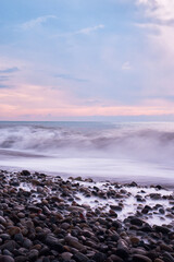 Obraz premium Beautiful sea landscape. Beautiful pink sunset sky over sea coast with pebble beach. Photo is frozen using long shutter speed.