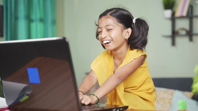 happy disabled Young girl kid laughing and clapping by looking fun online videos on laptop at home - concept of kids having fun during leisure time