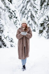 happy woman warming up with cup of tea in winter forest