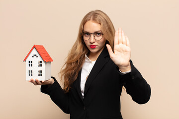 blonde woman looking serious, stern, displeased and angry showing open palm making stop gesture