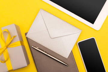 top view of smartphone and digital device with blank screen on copy book with golden pen and envelope near gift box isolated on yellow