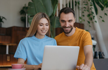 Portrait of young smiling couple using laptop computer, internet, communication, working from home. Happy students studying together, distance learning, online education, teamwork