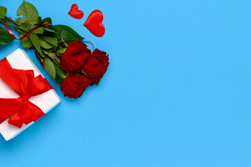 Happy Valentines day. Dating concept. Bunch of roses and gift box with red bow on blue background