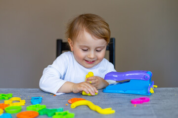 little child playing with placticine, dough, colorful modeling compound, sitting at table at home or kindergarten. Creative leisure with kids.