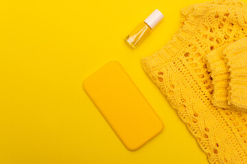 top view of bottle with nail polish, smartphone in case near jumper isolated on yellow