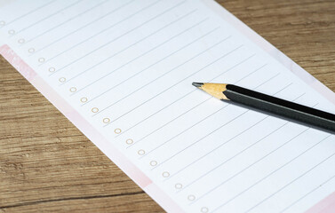 Black pencil on empty lined paper blank. Wooden table background. Close-up.