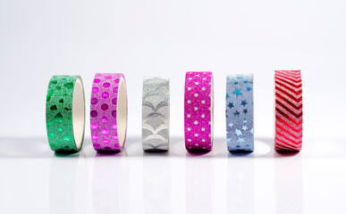 Several multicolored shiny rolls of adhesive packaging tape on a light background.