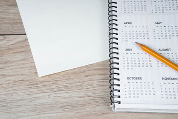 Top view of clean white paper blank, pencil and spiral calendar on wooden table background.