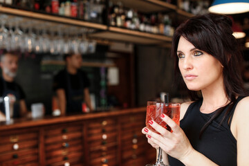 ragazza mora con gli occhi verdi ed espressione serie prende qualcosa da bere  in un bar 