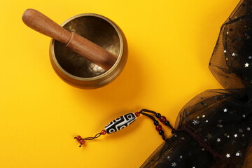 Tibetan Singing Bowl and Tibetan 9 Eyes Dzi Beads necklace on a yellow background, black fabric...