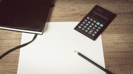 Personal leather bounded journal. Black pencil on empty paper blank. Calculator  on wooden table. Top view.